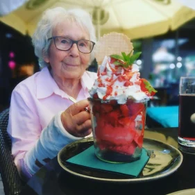 Ein Frau die glücklich vor einem großen erdbeerbecher mit Sahne sitzt